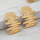 Oversized textured gold statement earrings displayed on a wooden surface showcasing their organic sculptural layered design.