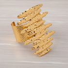 Flat lay of oversized hammered gold earrings and matching cuff bracelet on a white wooden background highlighting coordinated Afro-luxe styling.