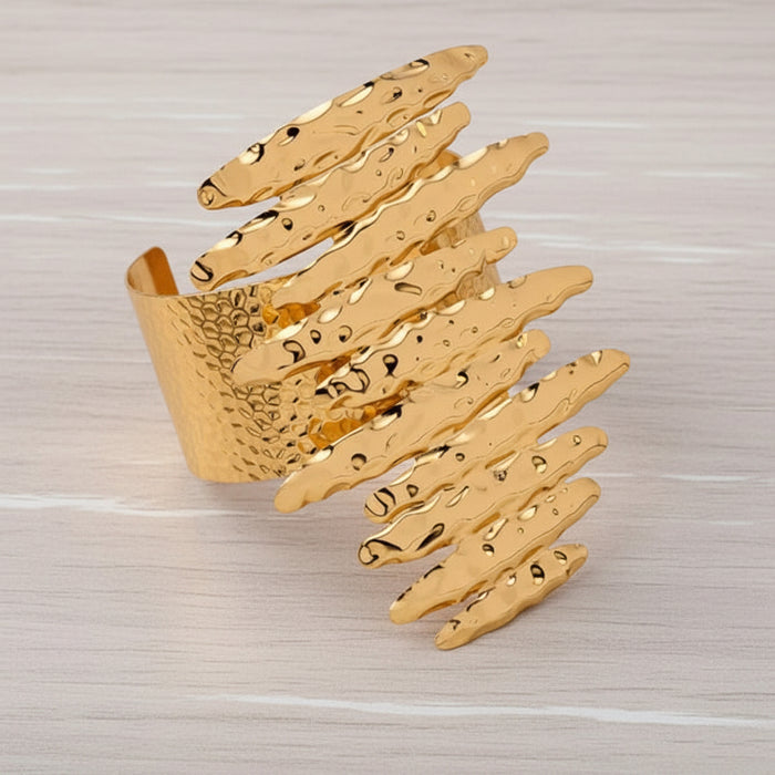Flat lay of oversized hammered gold earrings and matching cuff bracelet on a white wooden background highlighting coordinated Afro-luxe styling.