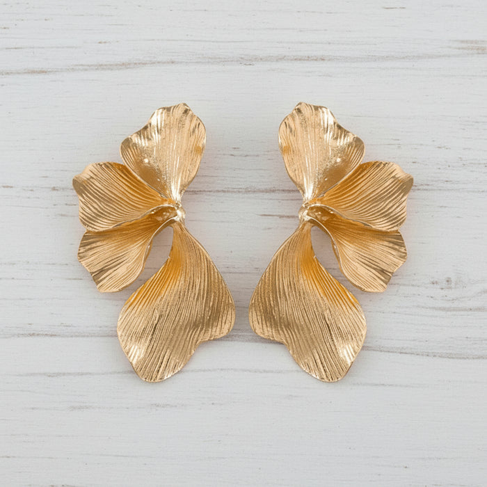 Pair of oversized 18K gold orchid statement earrings with sculptural floral petals and textured botanical design on a white background.