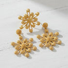 A gold jewelry set featuring a starburst-style brooch, earrings, and a matching necklace displayed on a dark brown rectangular stand against a white background.