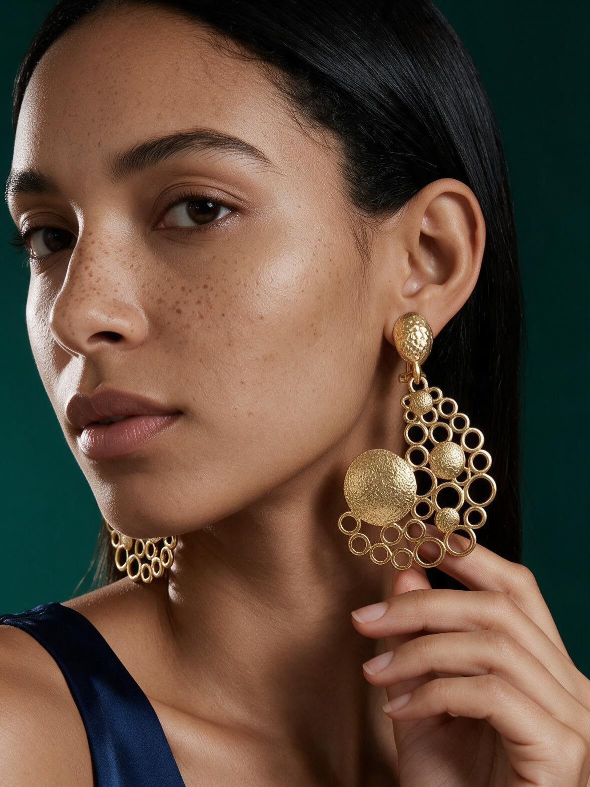 Lifestyle close-up of a model wearing lightweight gold bubble statement earrings paired with a sleek navy satin outfit.
