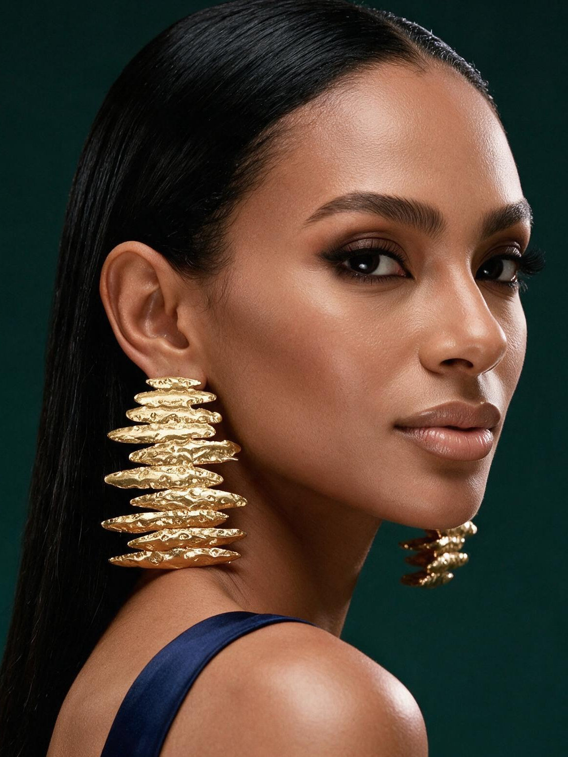 Model wearing oversized Afrocentric gold statement earrings with layered hammered texture and sculptural contemporary design.