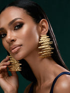 Model wearing oversized Afrocentric gold statement earrings with layered hammered texture and sculptural contemporary design.