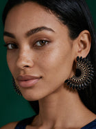 Black and gold oversized rhinestone statement earrings with floral geometric design worn by smiling model.