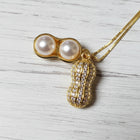 Close-up of a gold peanut pendant necklace featuring two luminous ivory pearls and sparkling moissanite accents on a fine gold chain.