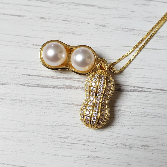 Close-up of a gold peanut pendant necklace featuring two luminous ivory pearls and sparkling moissanite accents on a fine gold chain.