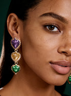 Close-up of oversized floral petal earrings featuring purple glitter, emerald green enamel, and gold accents worn by model.
