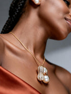 Close-up of a gold pearl peanut pendant necklace resting on a model's neckline, highlighting the textured shell design, sparkling moissanite, and luminous pearls.