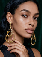 Portrait of a model wearing bold 18K gold plated African statement earrings showcasing elegant movement and lightweight luxury design with her fingers touching the earrings