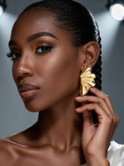 Side profile of a model wearing oversized gold botanical statement earrings inspired by Ginkgo leaves, highlighting the modern sculptural petal silhouette with her hand touching the earrings.
