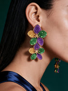 Close-up of oversized floral petal earrings featuring purple glitter, emerald green enamel, and gold accents worn by model.