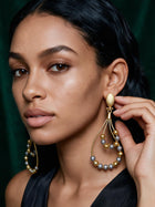 Portrait of a model wearing bold 18K gold plated African statement earrings showcasing elegant movement and lightweight luxury design with her fingers touching the earrings
