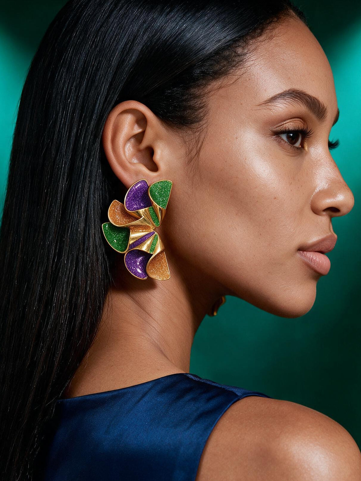 Woman wearing colorful New Orleans-inspired geometric stud earrings in purple, emerald green, and gold paired with an elegant emerald velvet high-neck top.