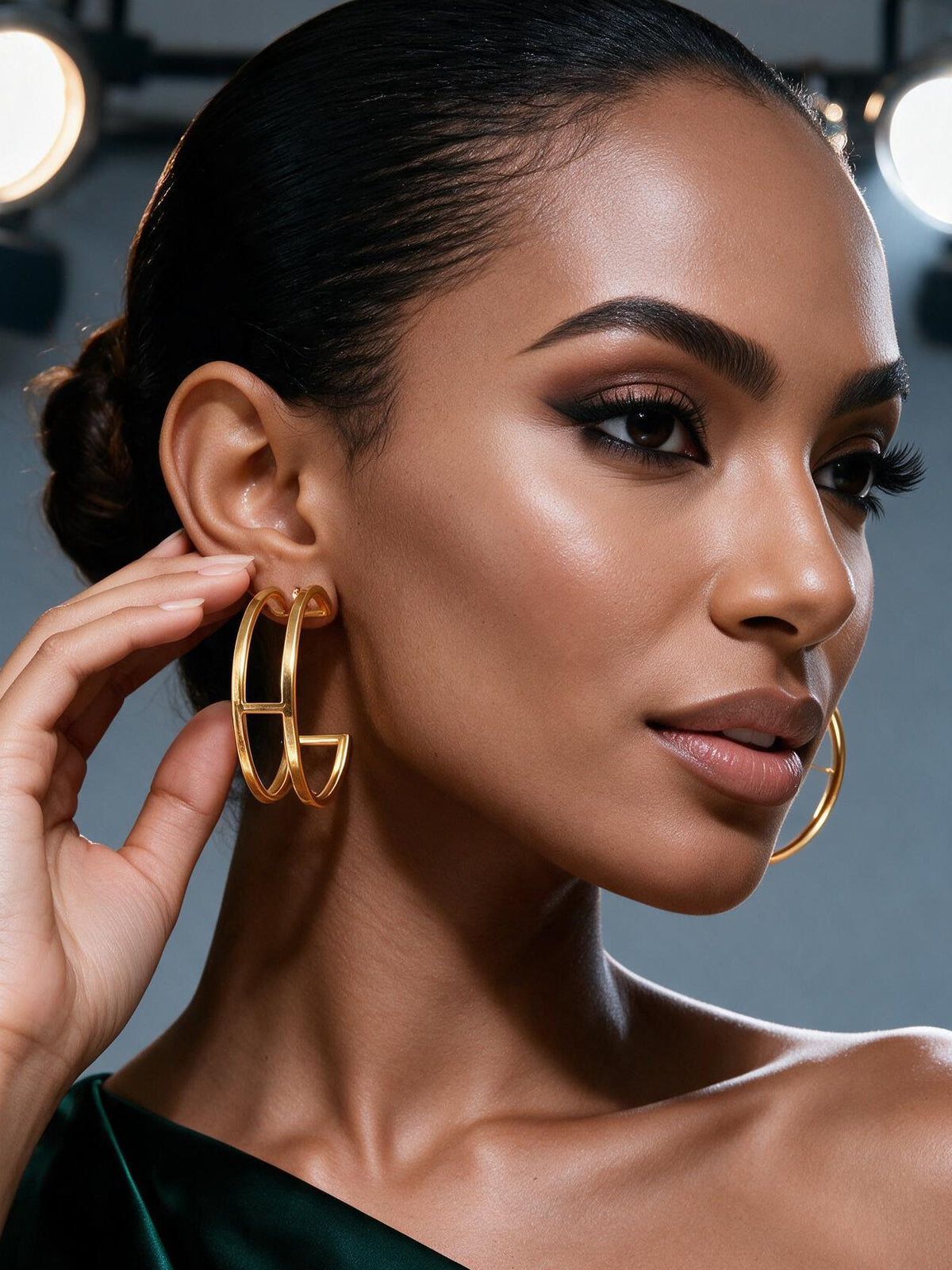 Black woman model Model wearing lightweight 18K gold plated sculptural round hoop earrings with a minimalist abstract design, styled with a sleek bun for a modern luxury look. Her hands her slightly touching earrings this Hypoallergenic & Nickel Free, Tarnish Resistant with Modern Sculptural Round Design Earrings. it is perfect for Everyday wear
,Workwear, Brunch dates, Vacation outfits, Wedding guests, Fashion influencers, Minimalist style lovers, Quiet luxury wardrobes, perfect Gift for mother