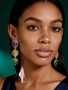 Close-up of oversized floral petal earrings featuring purple glitter, emerald green enamel, and gold accents worn by model.