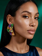 Model wearing vibrant Mardi Gras-inspired statement earrings featuring layered geometric shapes in purple, green, and gold for festival styling.
