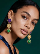 Model wearing colorful Mardi Gras-inspired flower statement earrings in purple, green, and gold with elegant green satin dress.
