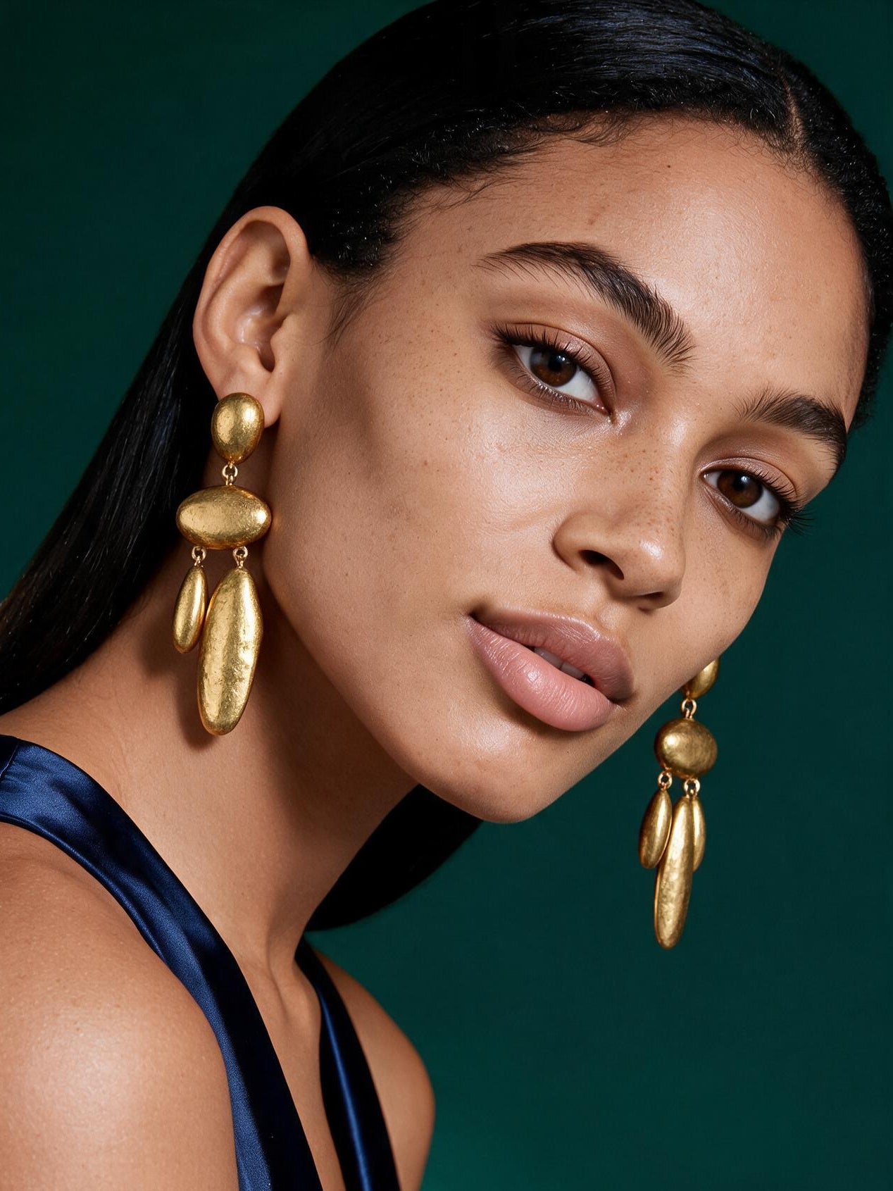 Model wearing oversized African-inspired gold waterdrop statement earrings styled with braided hair and natural glam makeup.