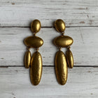 Large 18K gold-plated sculptural waterdrop dangle earrings displayed on a rustic wooden surface, featuring an elegant organic pebble-inspired design.