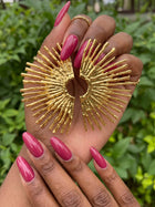 Oversized 18K gold plated sunburst statement earrings displayed in hand, featuring a sculptural fan design and textured stainless steel finish.