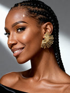Model wearing oversized gold sunburst fan stud earrings with a radiant geometric design, styled with braided hair for a luxury fashion look.