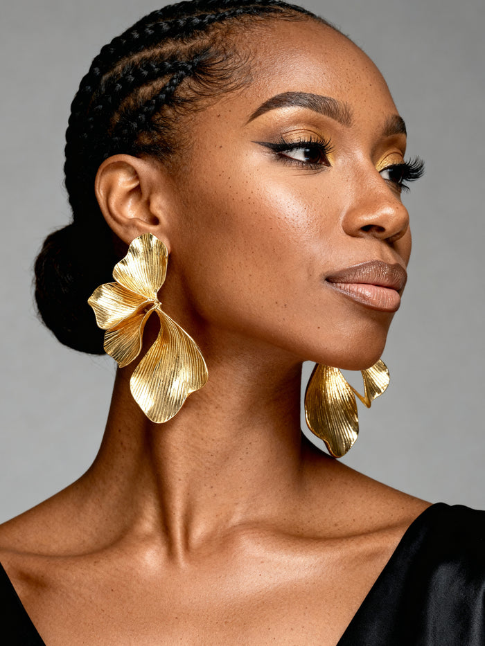 Black Woman wearing oversized gold orchid flower statement earrings with textured botanical petals, styled as elegant lightweight jewelry for weddings, vacations, and special occasions.