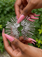 Silver sunburst statement earrings held by hand, showcasing the textured geometric fan design in polished stainless steel.