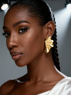 Model wearing lightweight 18K gold plated sculptural flower stud earrings with a brushed botanical texture, styled with braided hair and an elegant black off-the-shoulder top.