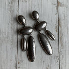 Gunmetal version of the sculptural waterdrop earrings displayed on a wooden background, showcasing the same modern organic silhouette.